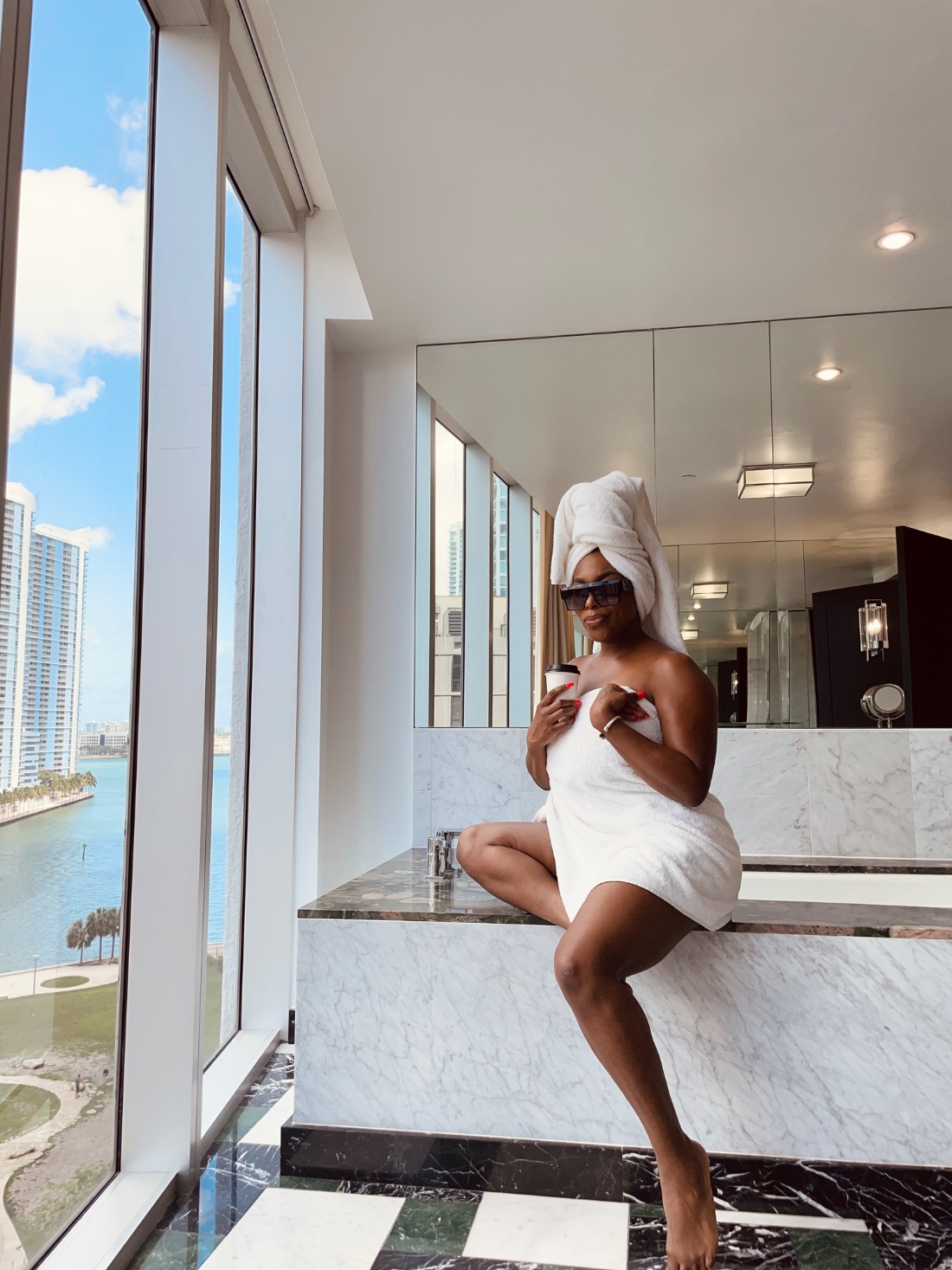India in a towel with morning coffee, marble bath overlooking the Miami waterfront