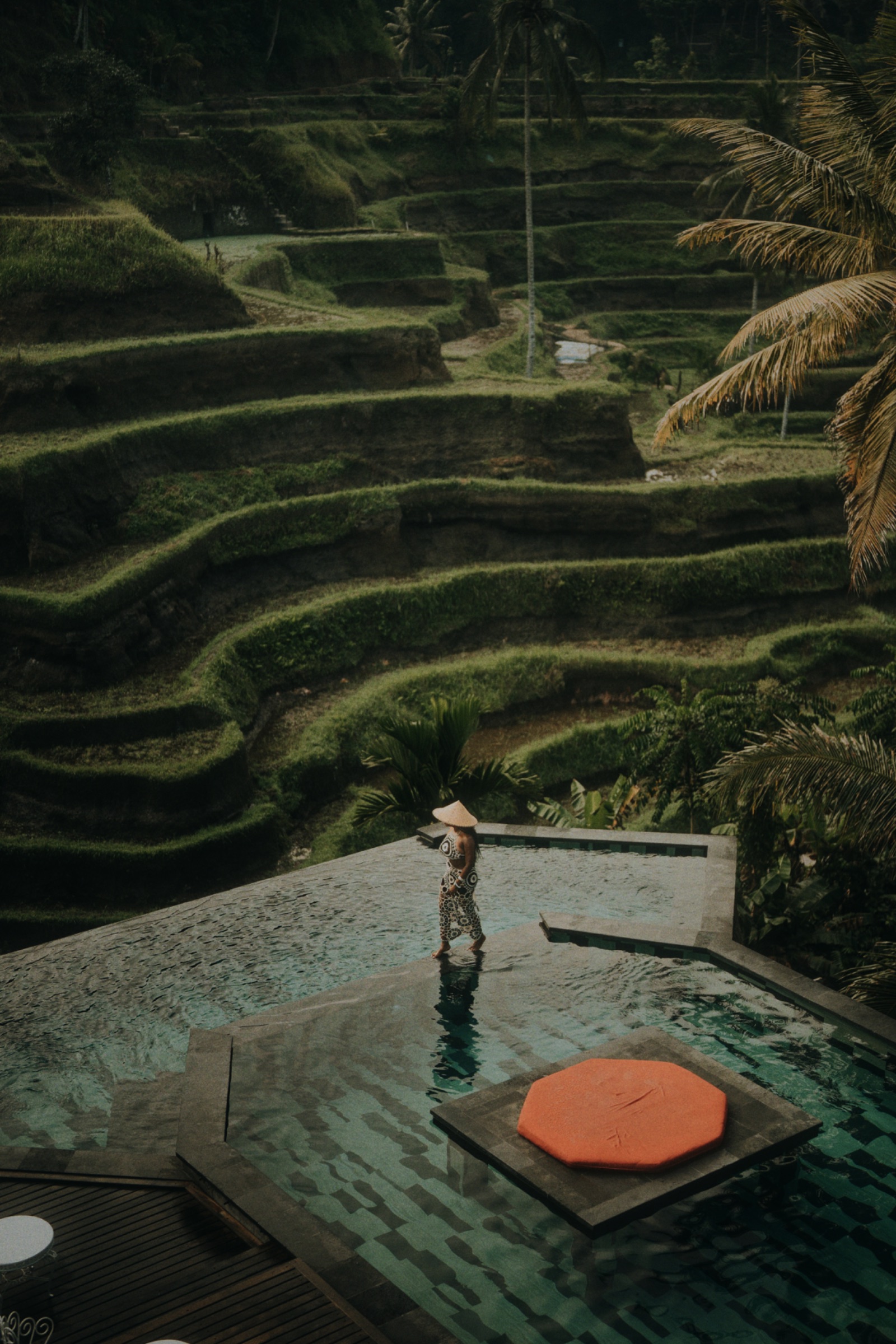 Aerial view of India walking the edge of a private infinity pool above the Tegallalang rice terraces